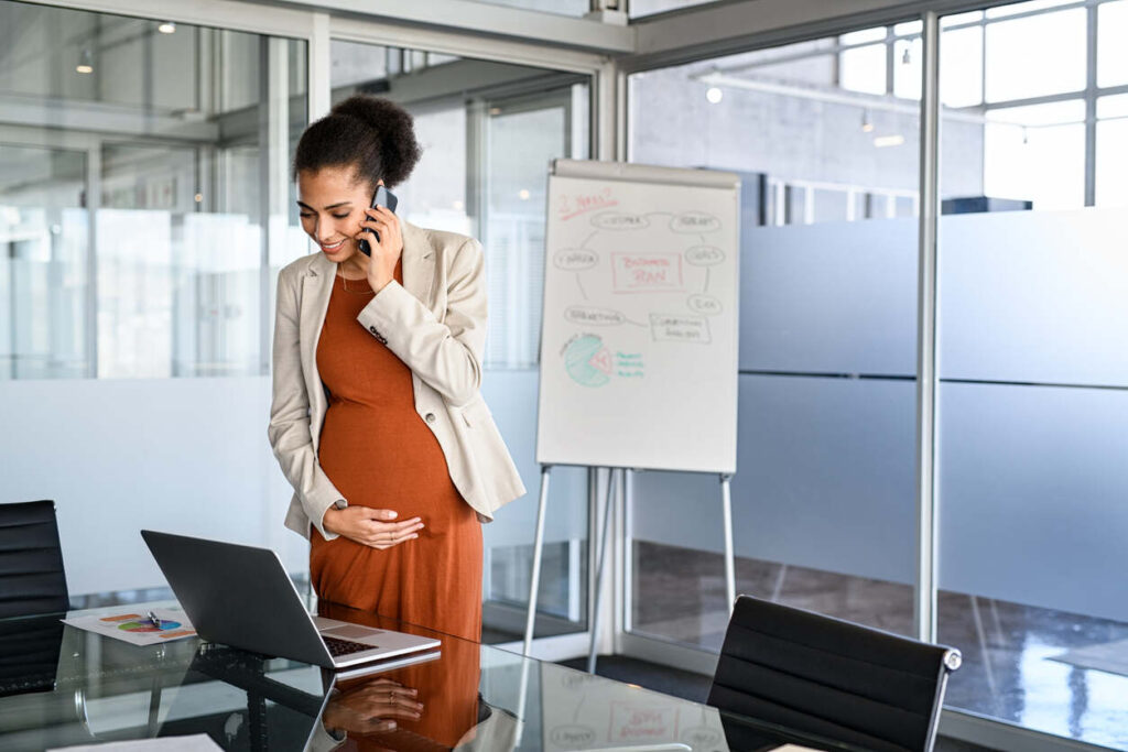 A pregnant professional on the phone, working at a laptop in an office, symbolizing maternity leave and workplace rights for expectant mothers in California