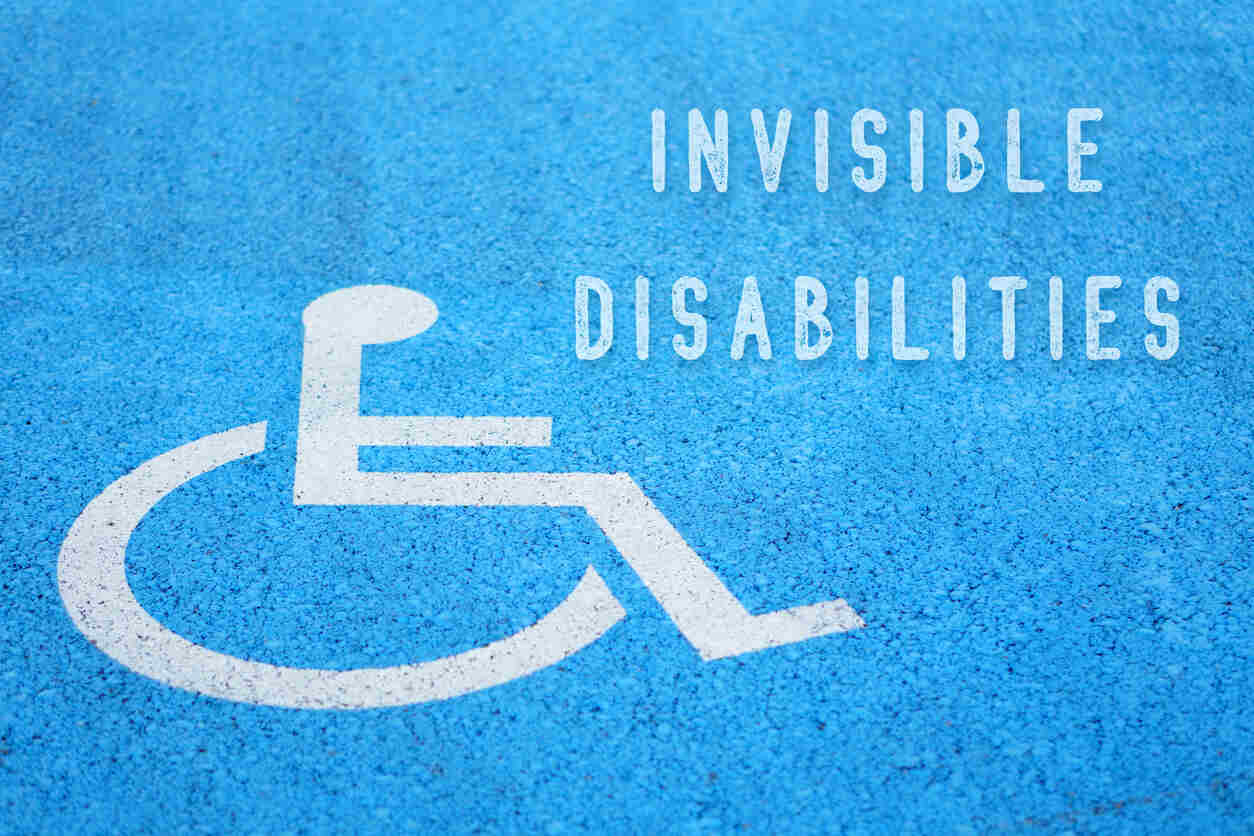 Blue painted parking spot with a white wheelchair symbol and "INVISIBLE DISABILITIES" text, highlighting workplace discrimination issues in California.