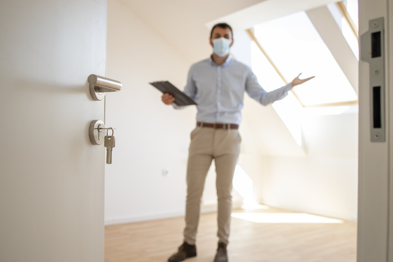 Out-of-focus individual in an empty room, holding documents and appearing to discuss a property issue, relevant to reporting landlord violations.