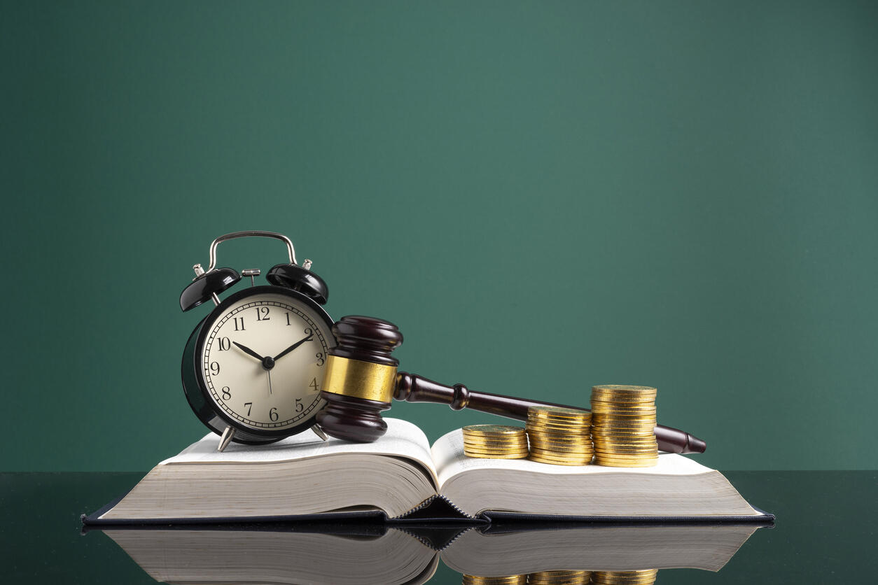 A gavel and a stack of gold coins on an open book next to an alarm clock, symbolizing legal cases and compensation for wage and hour laws.