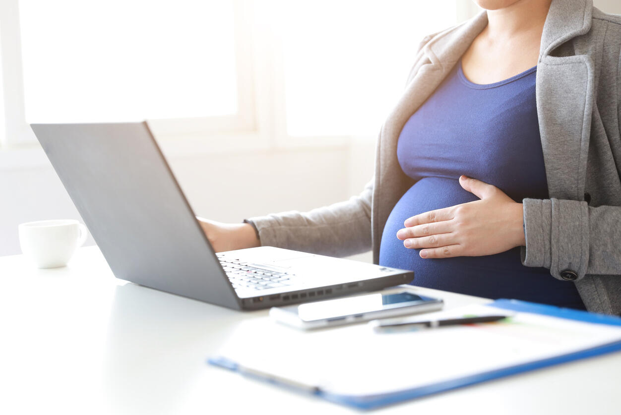Pregnant woman working on a laptop, symbolizing maternity leave rights and potential demotion issues.