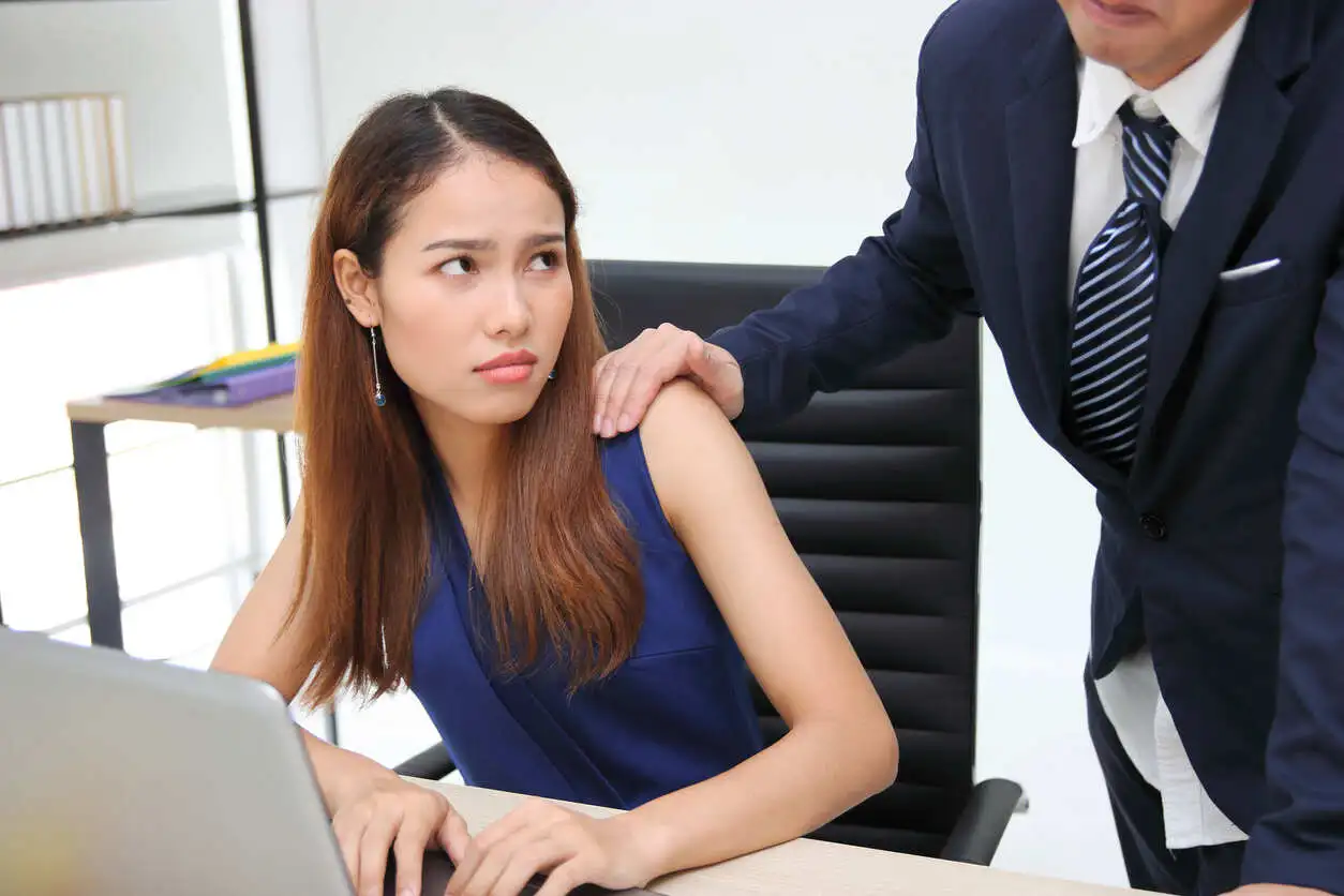 Employee looking uncomfortable as a colleague in a suit places his hand on her shoulder, illustrating a sexual harassment situation.