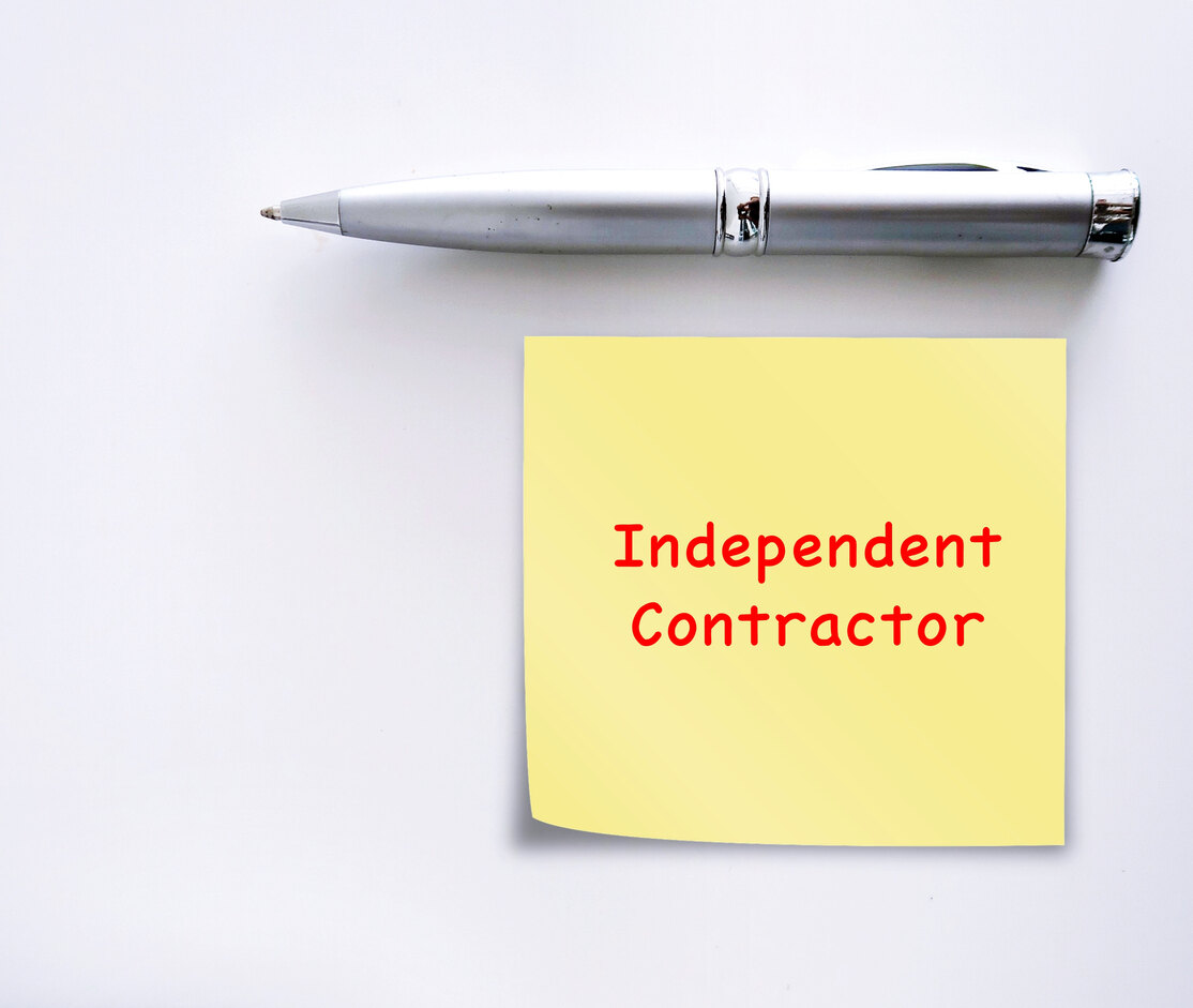 A silver pen next to a yellow sticky note reading ‘Independent Contractor’ in red text on a white background.